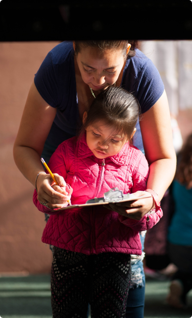 Our Impact photo header showing a volunteer leading a girl through writing exercises